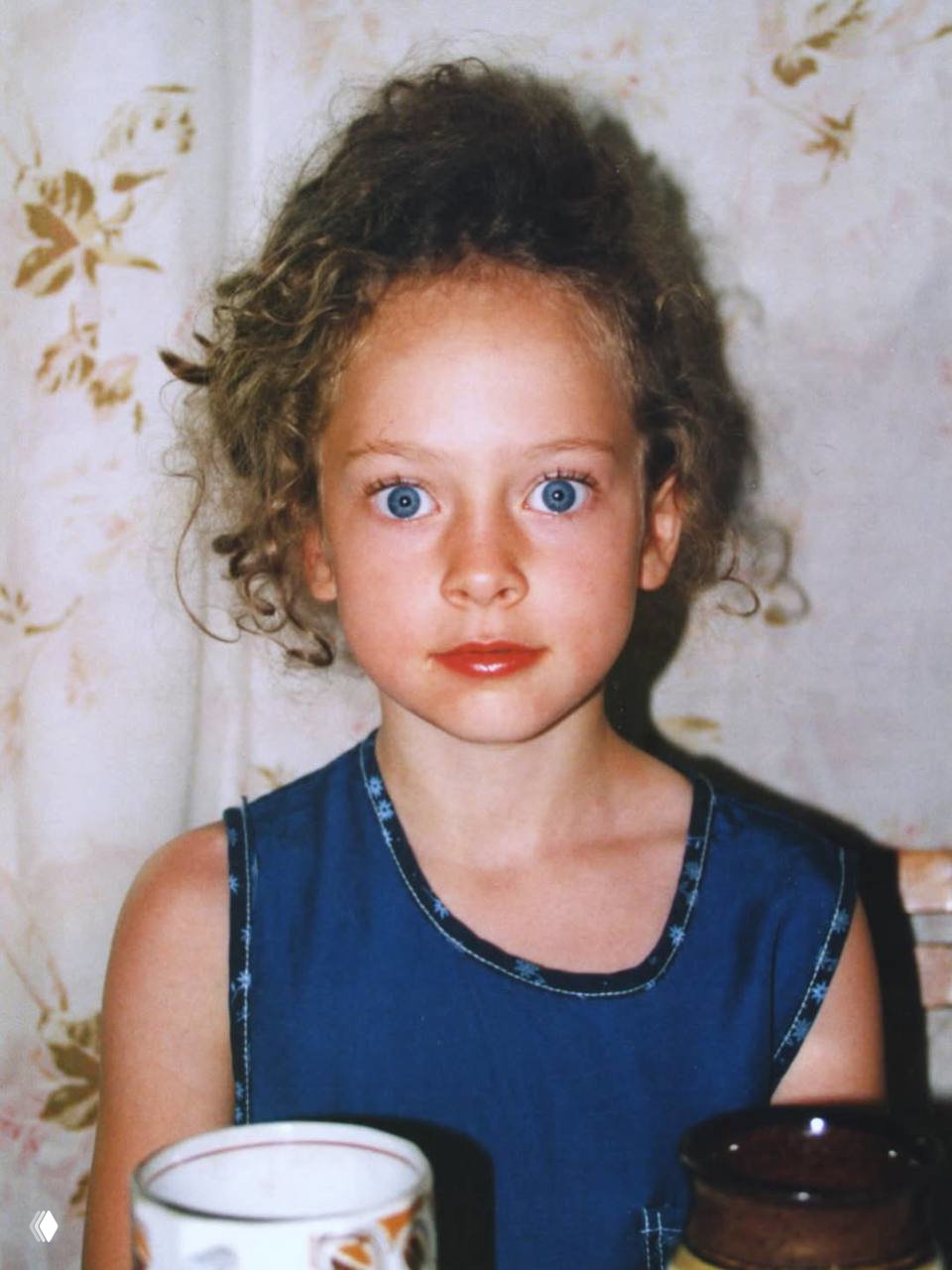 Цветное детское фото Аглаи Тарасовой в платье, крупный план с выразительными голубыми глазами и вьющимися волосами.