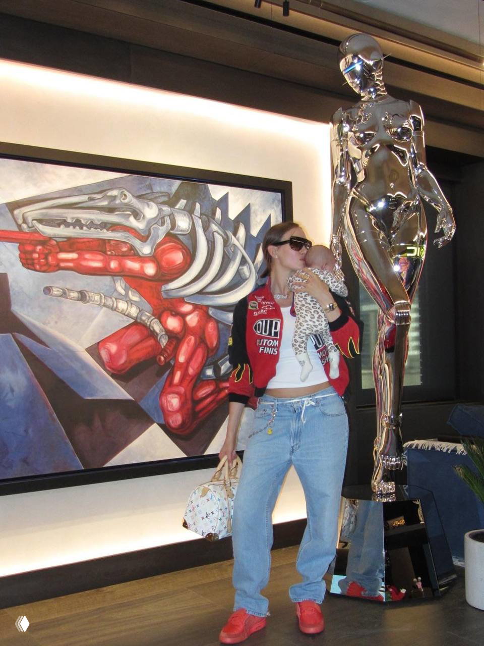 Женщина держит ребёнка рядом с хромированной скульптурой и большим живописным полотном в холле с художественным декором