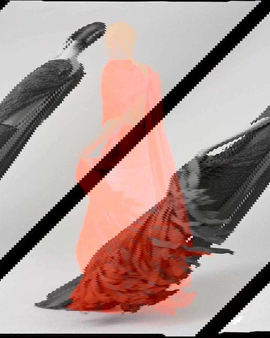 Джулианна Мур снята со спины в летящем складчатом красном платье; движение ткани подчёркивает силуэт и драматичный образ для журнала.