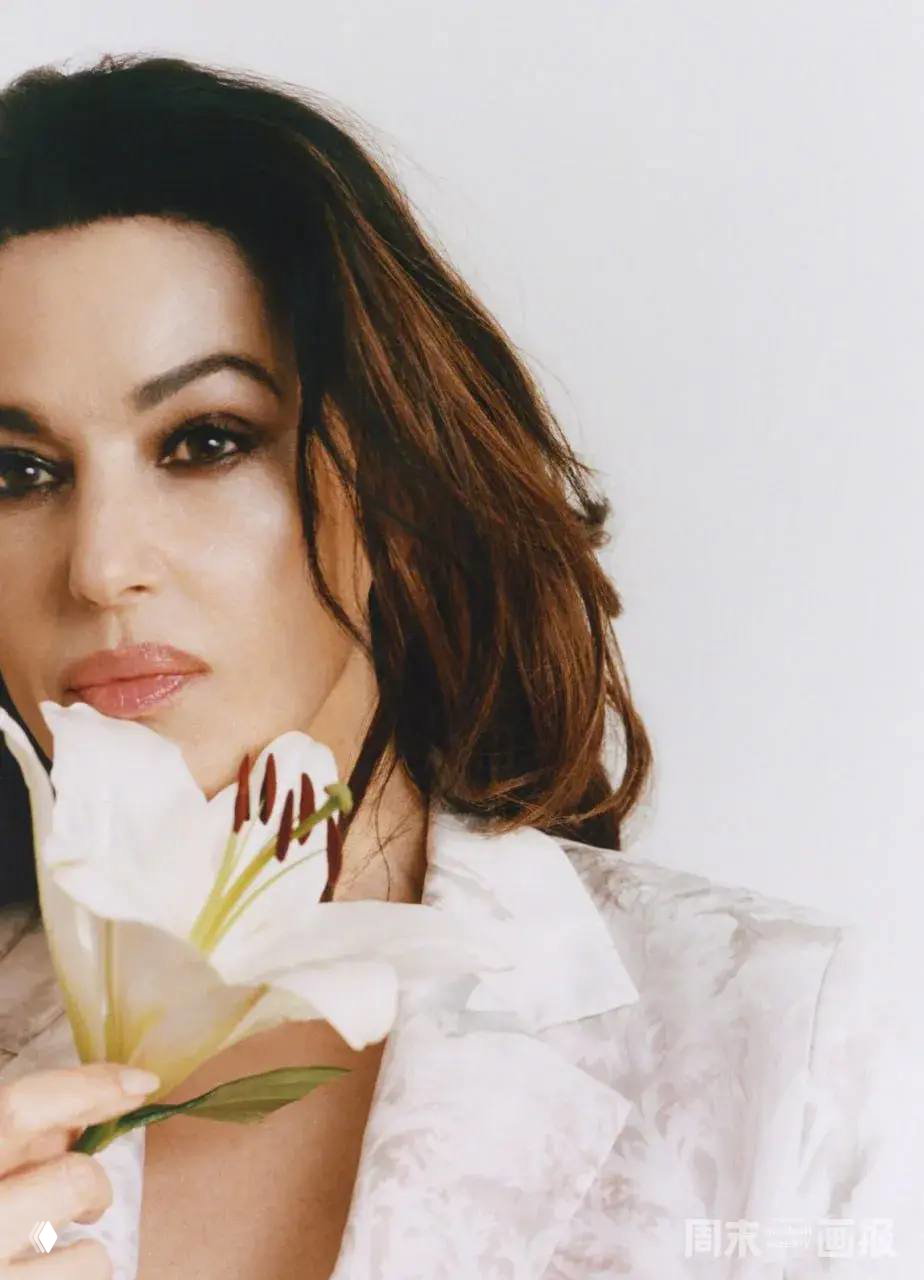 Крупный план Моники Беллуччи с белой лилией в руках, мягкий макияж и светлый фон — кадр из апрельской фотосессии для глянца.