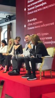 Участники и спикеры на красной сцене: кадр в профиль, видны микрофоны, мебель и фрагмент брендированного баннера сбоку.