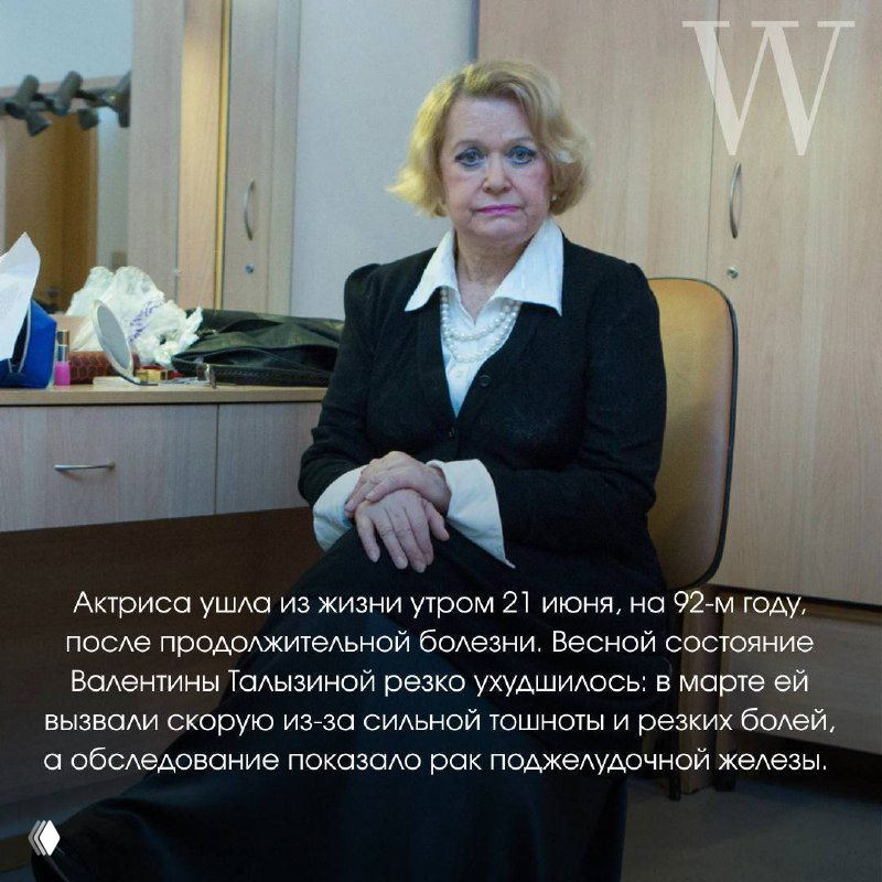 Чёрно-белая фотография пожилой женщины в деловом костюме, сидящая в помещении с мебелью на заднем плане, крупный план