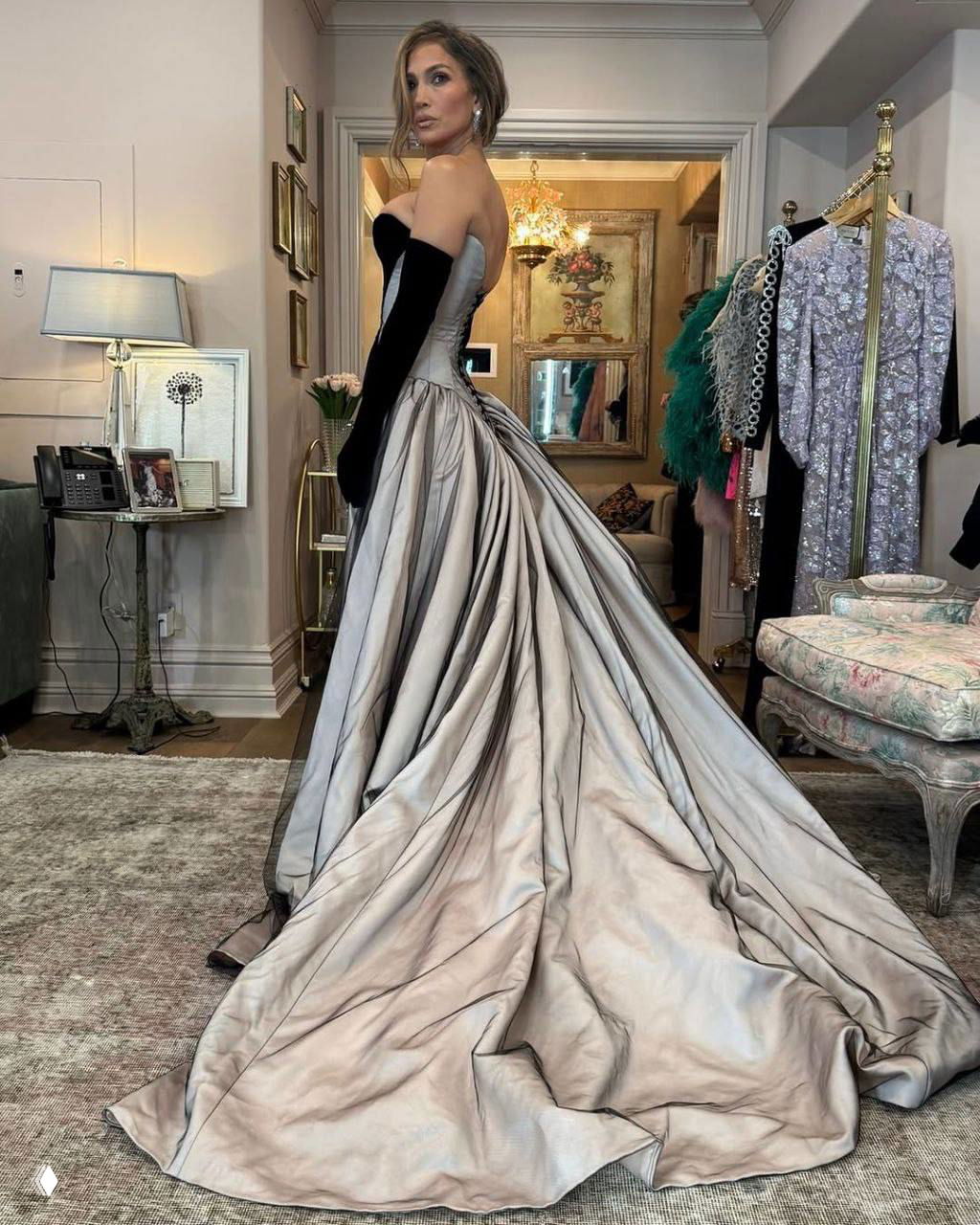 Дженнифер Лопес в полный рост в платье Tamara Ralph: приталенный корсет и развевающийся драпированный подол на фоне гардероба.