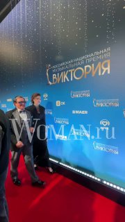 Двое гостей идут по красной дорожке мимо синей фотозоны с надписью «Виктория», на заднем плане видны логотипы спонсоров и освещение.