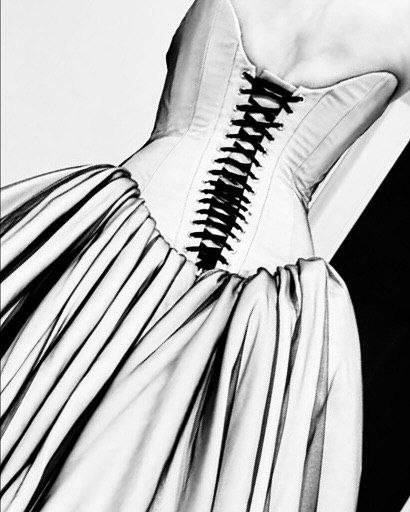 Чёрно‑белая фотография крупным планом корсета со шнуровкой и сборками ткани у талии, фрагмент детали платья.