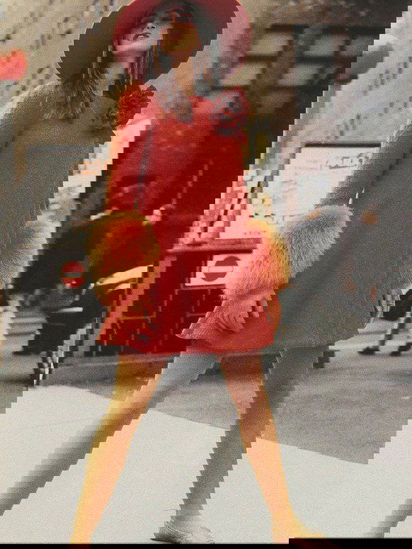 Уличный архивный кадр: модель в красном платье с шляпой и пушистыми манжетами идёт по городу в ярком винтажном образе 1990‑х.