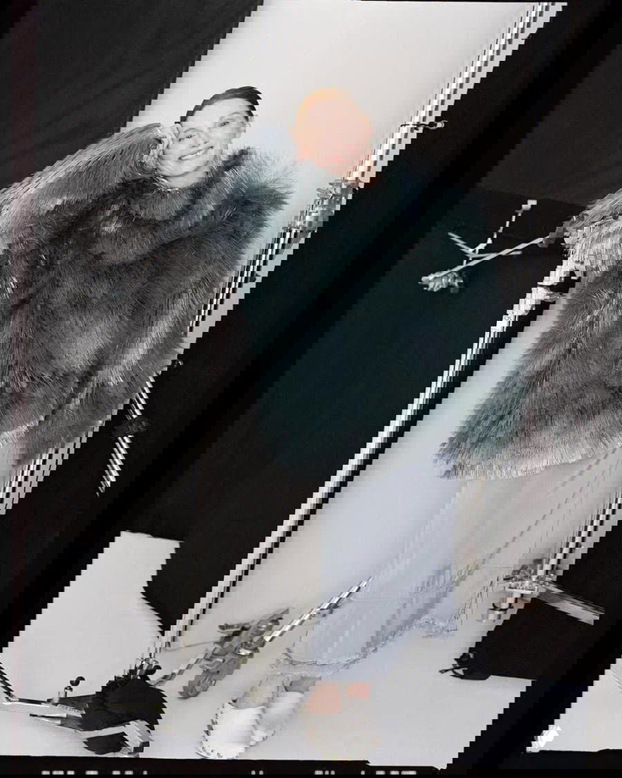 Джулианна Мур улыбается в студии в серой пушистой шубе и лёгкой юбке, на заднем плане студийное оборудование, закадровая атмосфера съёмки.