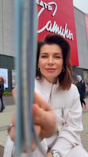 Екатерина Волкова у входа в театр в светлой куртке: улыбается на фоне фасада с вывеской Театр Сатиры, кадр уличной съёмки с телефоном в руках.
