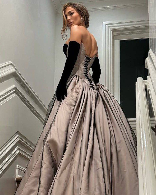 Вид со снизу: Дженнифер Лопес в корсетном платье и чёрных перчатках, подъём по лестнице и развёрнутый подол платья.