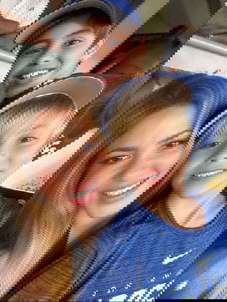 Селфи в зрительном зале: улыбающаяся женщина с двумя мальчиками в синей одежде, портретный тёплый семейный кадр во время мероприятия.