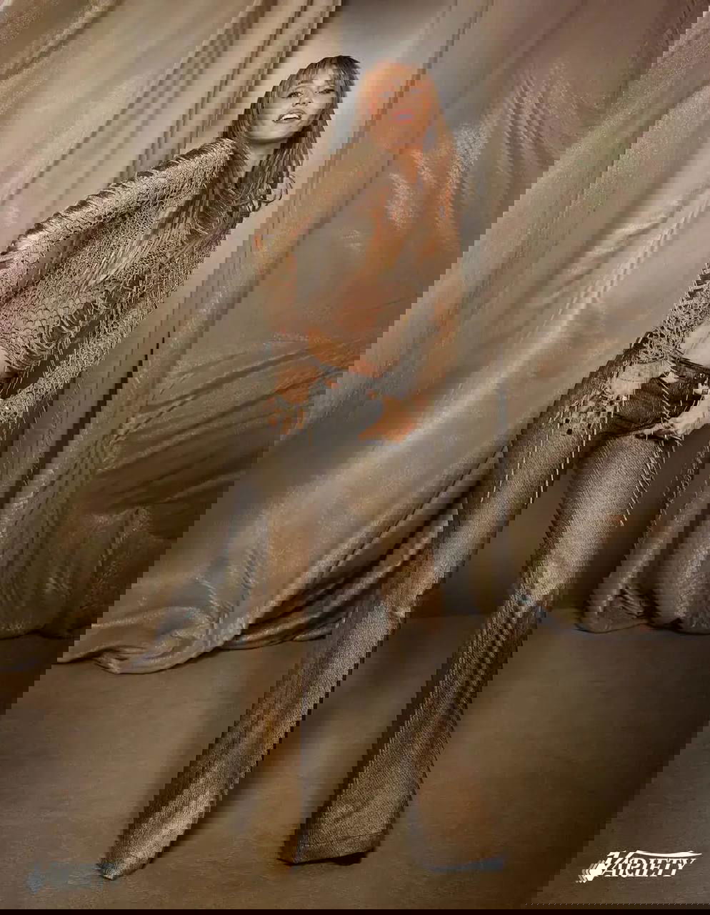 Майли Сайрус в золотистом сетчатом свитере и расклешённых брюках на фоне драпировок; ретро‑стилизация и позирование для портрета Variety.