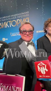 Мужчина в смокинге на красной дорожке у фотозоны музыкальной премии «Виктория», видны логотипы мероприятия и яркая сценическая подсветка.