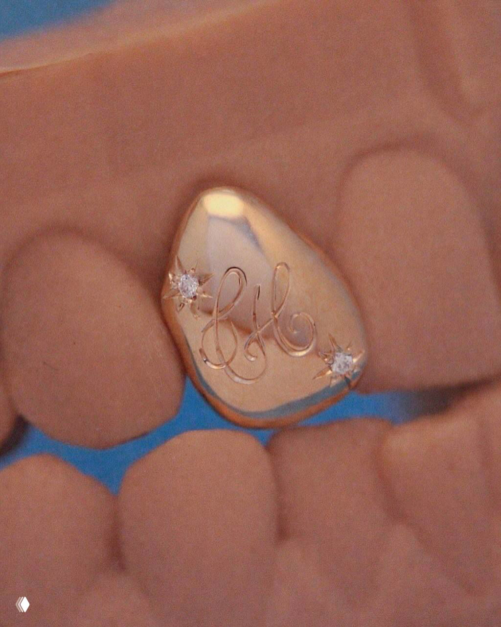 Крупный план золотой накладки на зуб с выгравированными инициалами и двумя маленькими бриллиантами на фоне губ.