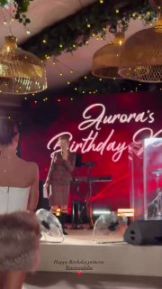 Широкий план сцены с ведущей и сценическим оформлением: надпись с названием праздника и световое оформление вечером.