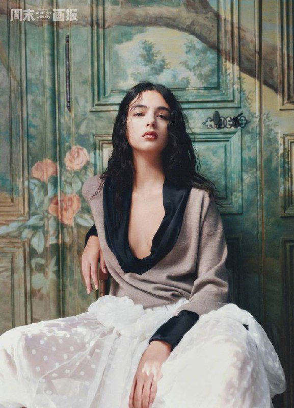 Модель сидит на стуле на фоне расписных дверей, свободная поза в прозрачной юбке — атмосфера романтической фешн-съёмки.