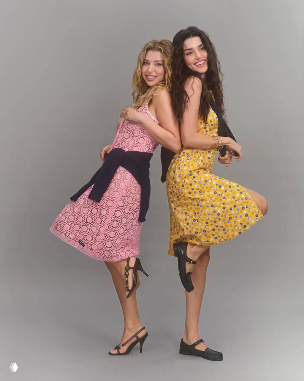 Динамичная студийная фотография: две модели в лёгких платьях танцуют и смеются на нейтральном фоне — фэшн-кадр.