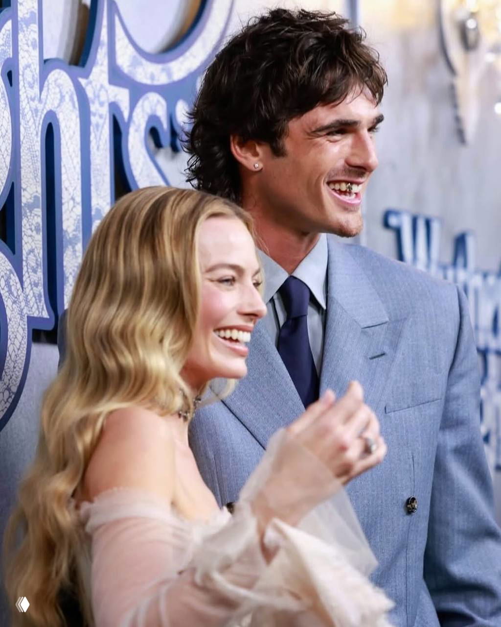 Два человека на красной дорожке: мужчина в костюме и женщина рядом улыбаются; видно золотое украшение на зубе мужчины.