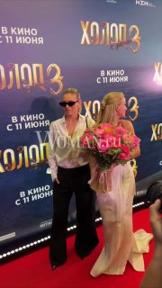 Кристина Асмус принимает поздравления с премьерой, держит букет, рядом гости и фотографы на фоне постера фильма и логотипов спонсоров.
