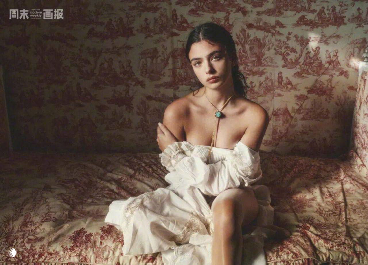 Портретная фотография модели на кровати с богатым текстильным фоном, лёгкий ретро-ансамбль и естественный свет.