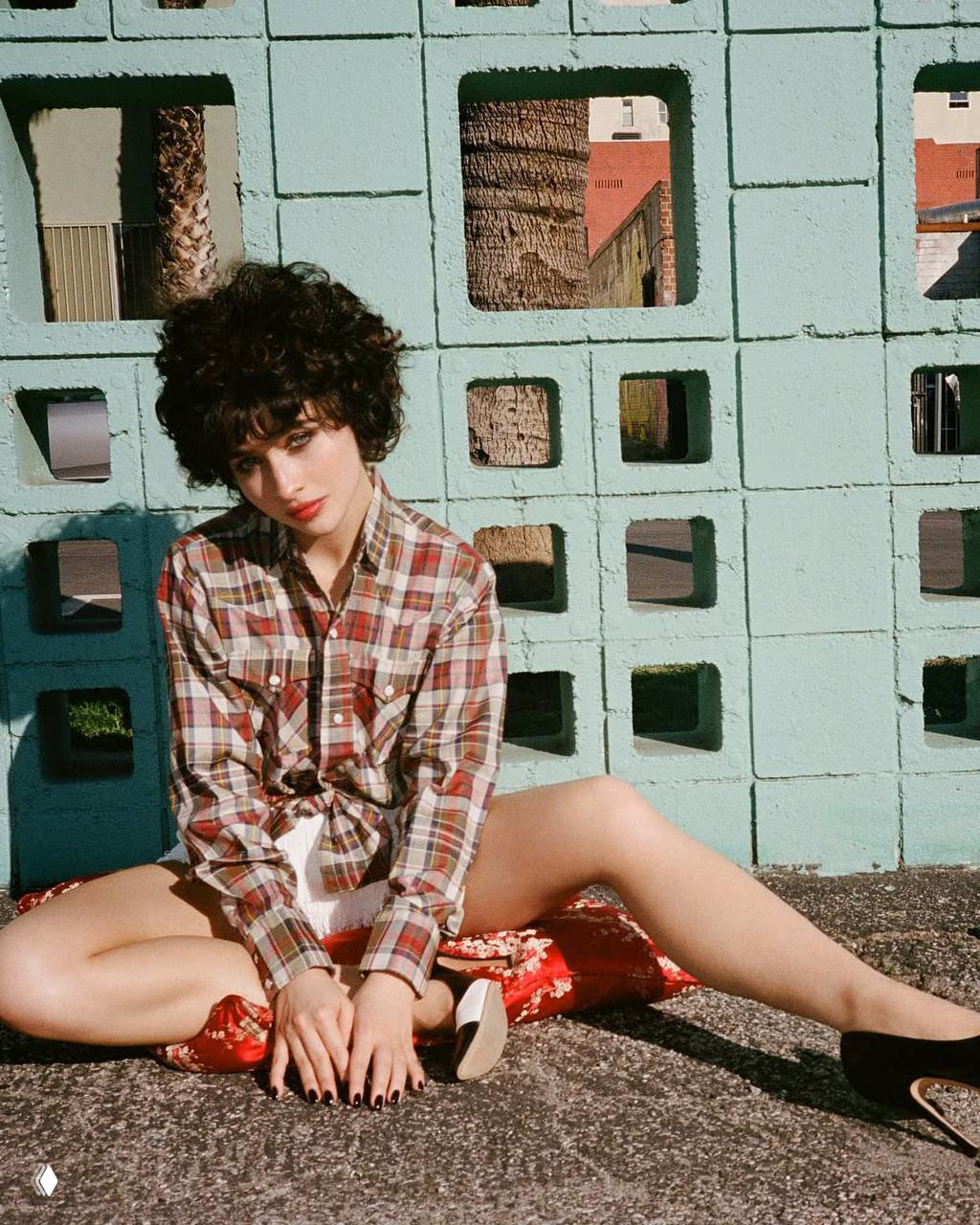 Сабрина Карпентер сидит у декоративной стенки в образе для обложки Perfect: расслабленная поза, модный лук и городской фон.