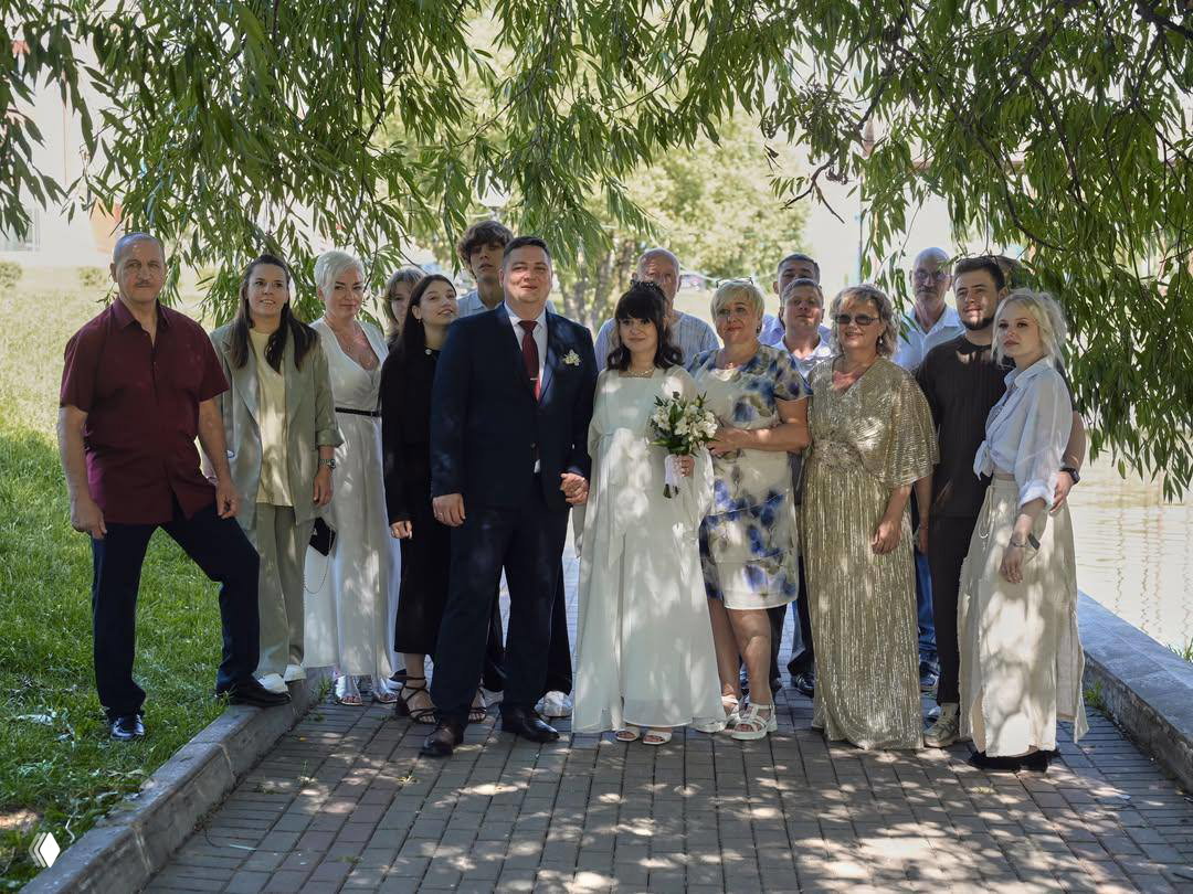 Групповое фото: Анна Руднева с женихом и родственниками стоят на дорожке в тени деревьев после свадьбы.