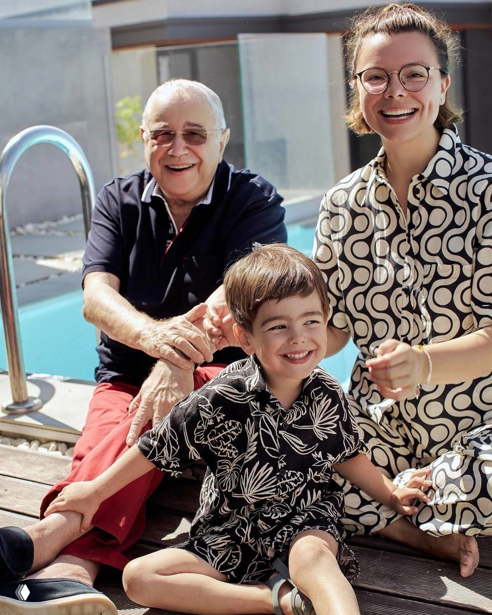 Семейная уличная фотография: мужчина, женщина и маленький мальчик улыбаются у бассейна в солнечный день, расслабленная повседневная сцена.