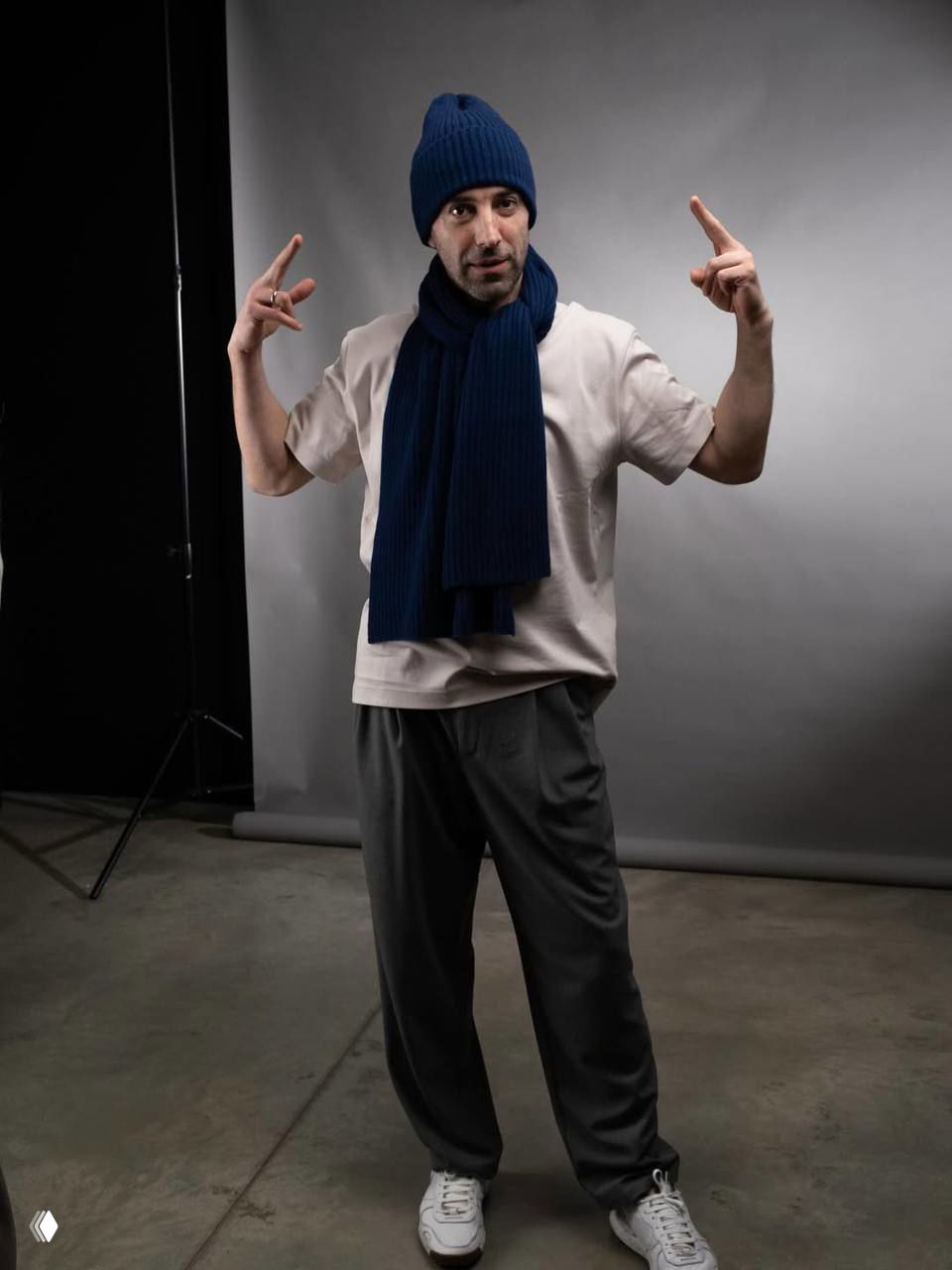 Портрет мужчины в студийной съёмке: полный рост, тёплая одежда, нейтральный фон и непринуждённая поза, художественный характер кадра.