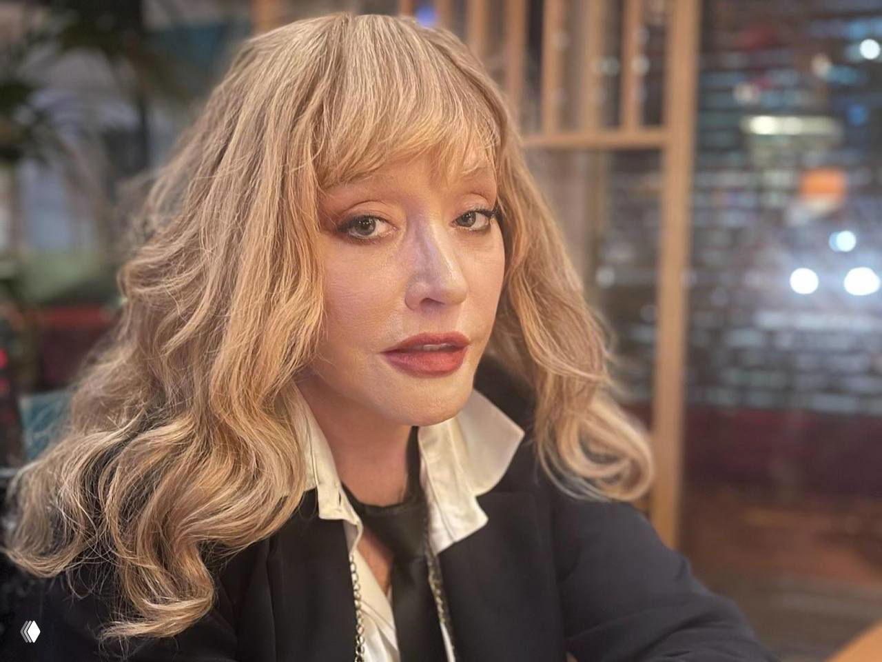 Крупный план взрослой женщины с причёской и макияжем в интерьере кафе или студии — портретная фотография в тёплой цветовой гамме.