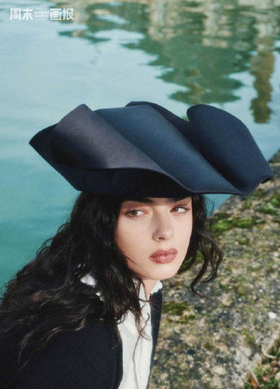 Крупный план лица модели на фоне воды, акцент на макияже и текстуре шляпы в модной фотосессии на природе.