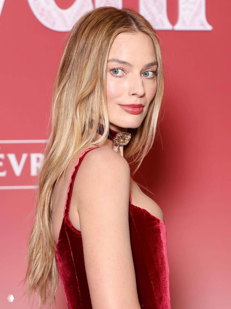 Крупный портрет Марго Робби на красной дорожке: светлые волосы, нюдовый макияж и бордовая помада в элегантном корсетном платье.