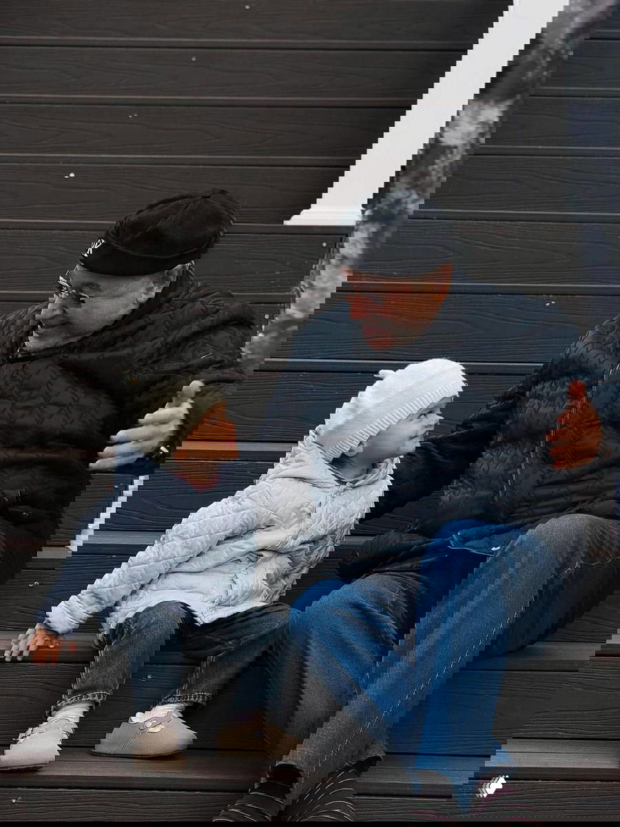 Сцена на ступеньках: пожилой мужчина сидит рядом с маленьким ребёнком в тёплой одежде, момент близкого общения и заботы между поколениями.