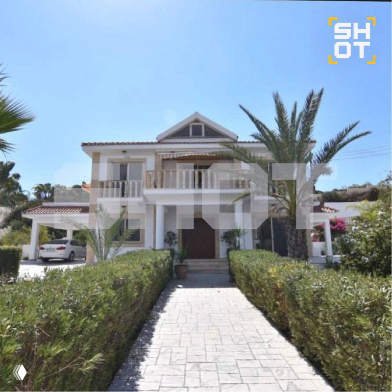 Частично искажённый цифровыми артефактами снимок фасада виллы с подъездной дорожкой, растительностью и видом на входную зону участка