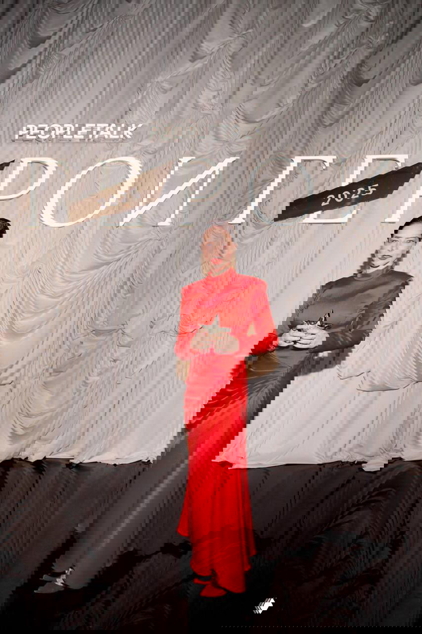 Женщина в длинном ярко-красном платье держит статуэтку на фоне драпировки и логотипа PEOPLETALK — кадр с церемонии награждения 2025.