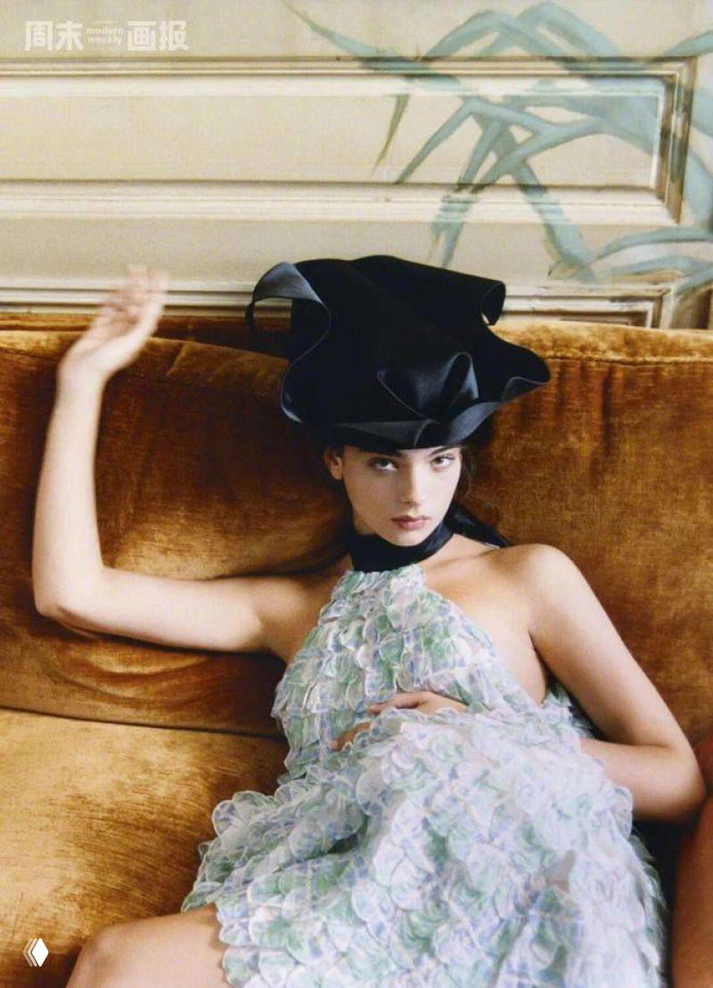 Модель в лёгком платье лёжа на диване в расслабленной позе, стилизованная съёмка с интерьерными текстурами.