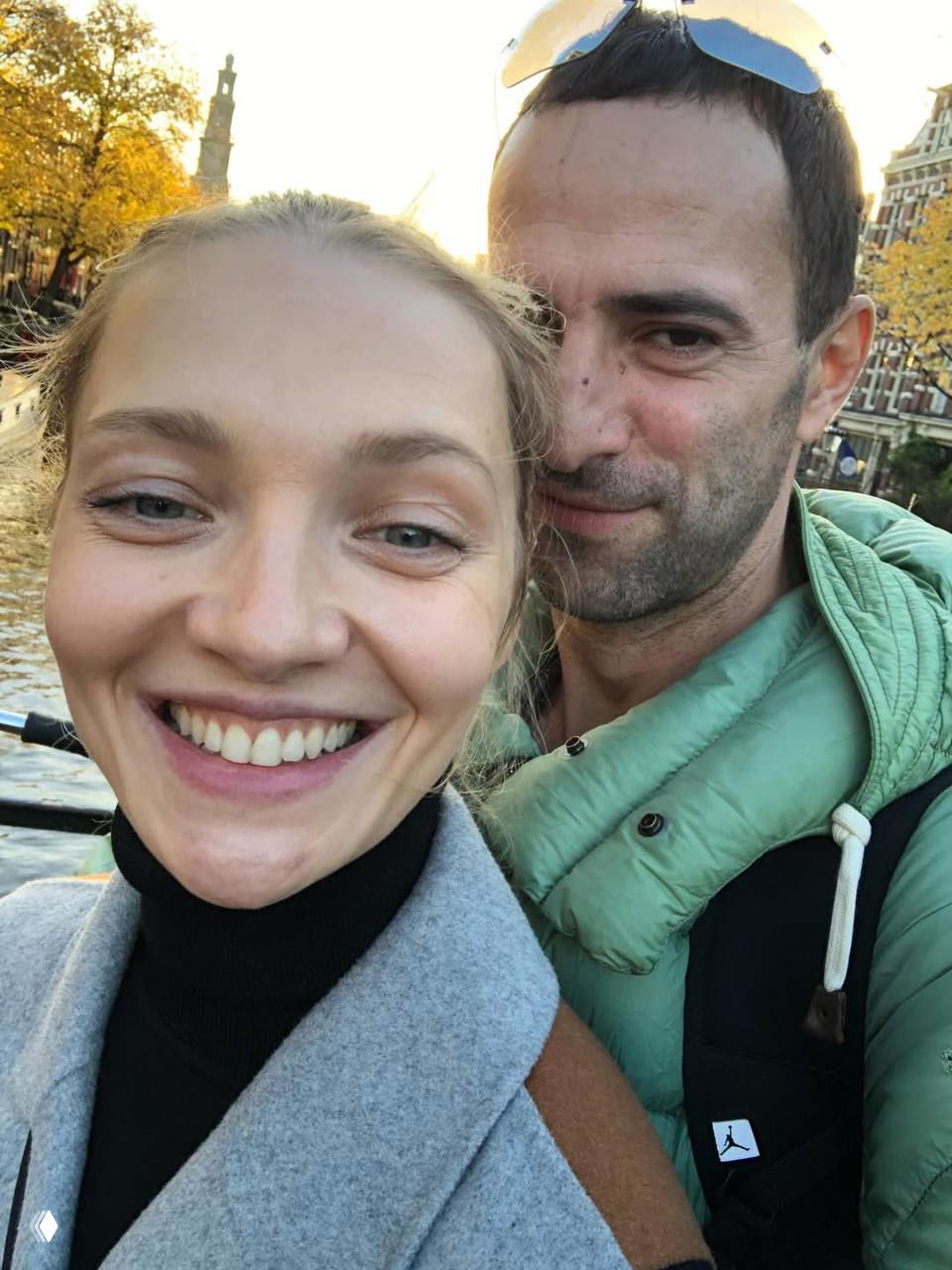 Селфи двоих людей на фоне городской набережной в осеннем свете; кадр передаёт непринуждённость прогулки и тёплые отношения.