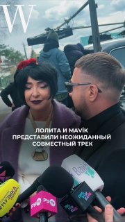 Кадр со съемочной площадки клипа: певица в темной стрижке дает интервью рядом с артистом в очках и микрофонами.