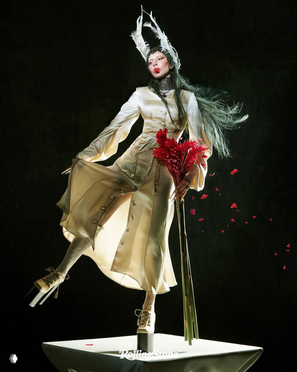 Леди Гага в светлом платье держит букет красных цветов, стоит на подиуме как театральная инсталляция — один из сценических кадров кавер-стори для Rolling Stone.