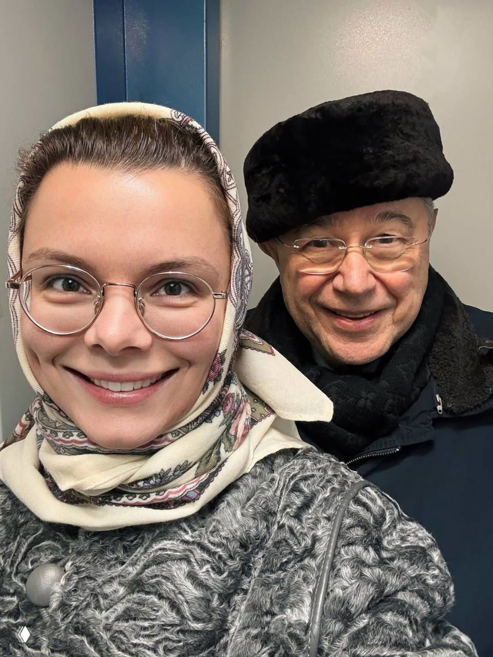 Селфи женщины в платке рядом с улыбающимся пожилым мужчиной на нейтральном фоне — семейный праздничный кадр без указания имён и персональных данных.