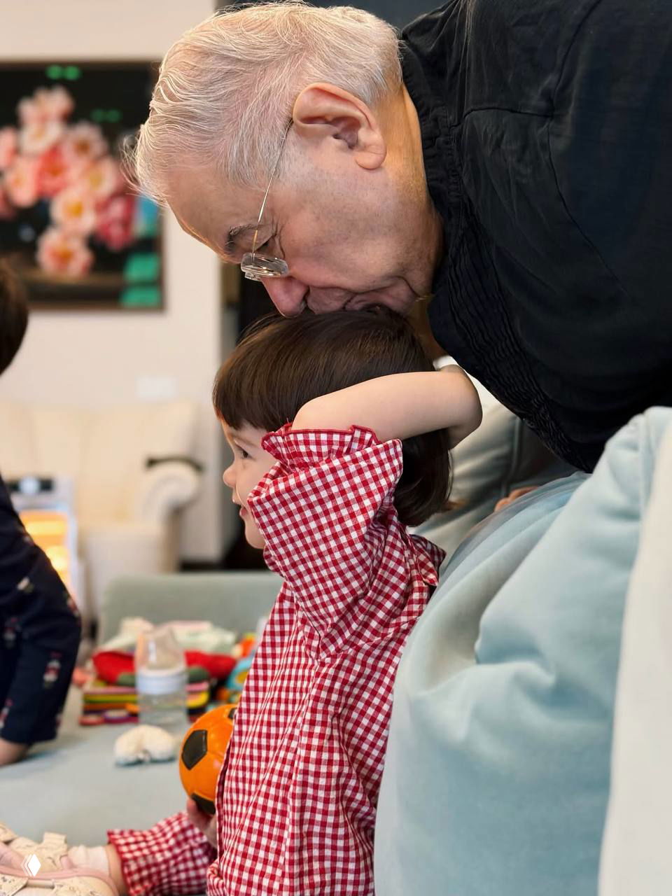 Пожилой мужчина наклоняется и целует голову ребёнка в клетчатой рубашке в домашней обстановке — искренний семейный момент в рождественской обстановке.