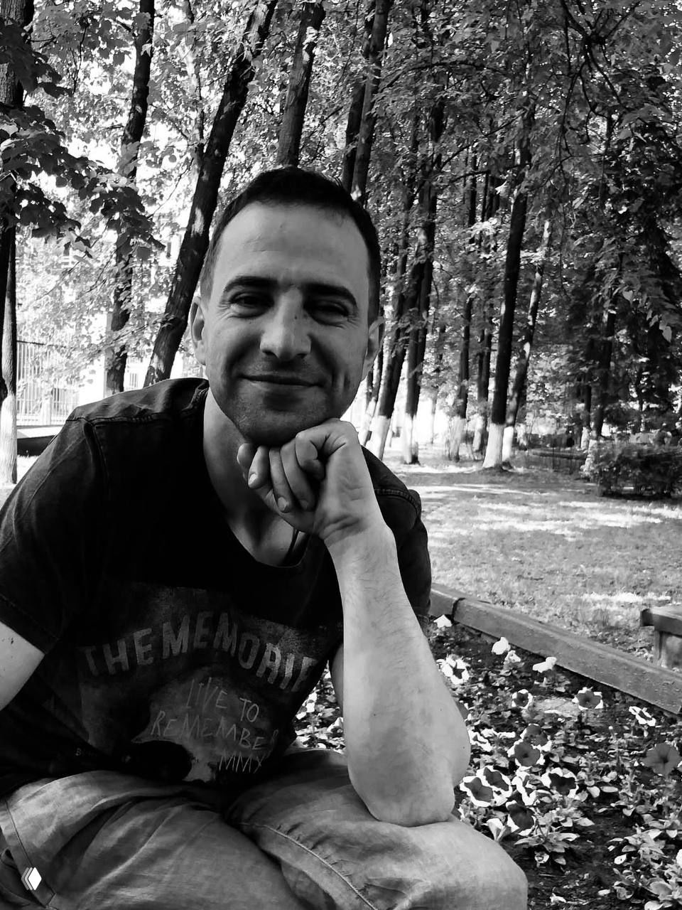 Чёрно‑белый портрет мужчины на скамейке в лесопарке: задумчивый взгляд, естественная поза и спокойная атмосфера снимка.