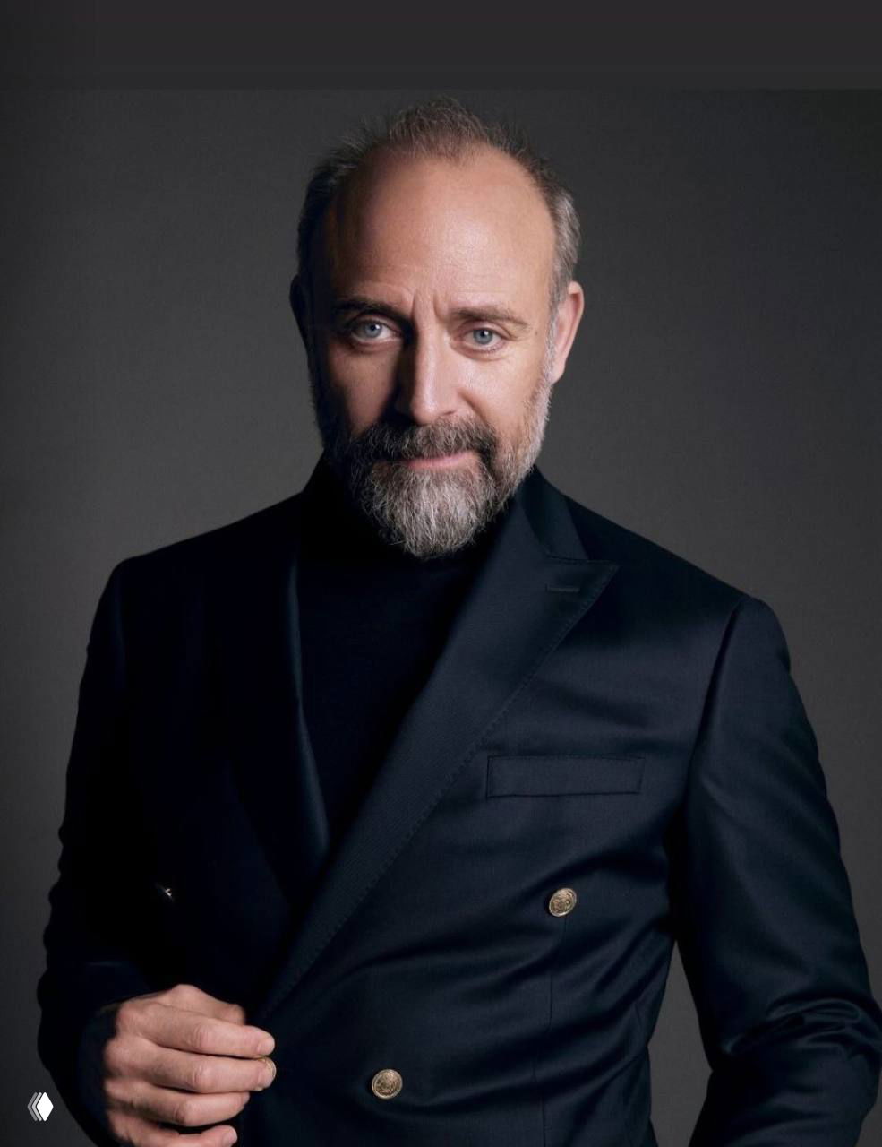 Крупный студийный портрет Халита Эргенча в тёмном пиджаке, с бородой и серьёзным, доброжелательным выражением на нейтральном фоне.