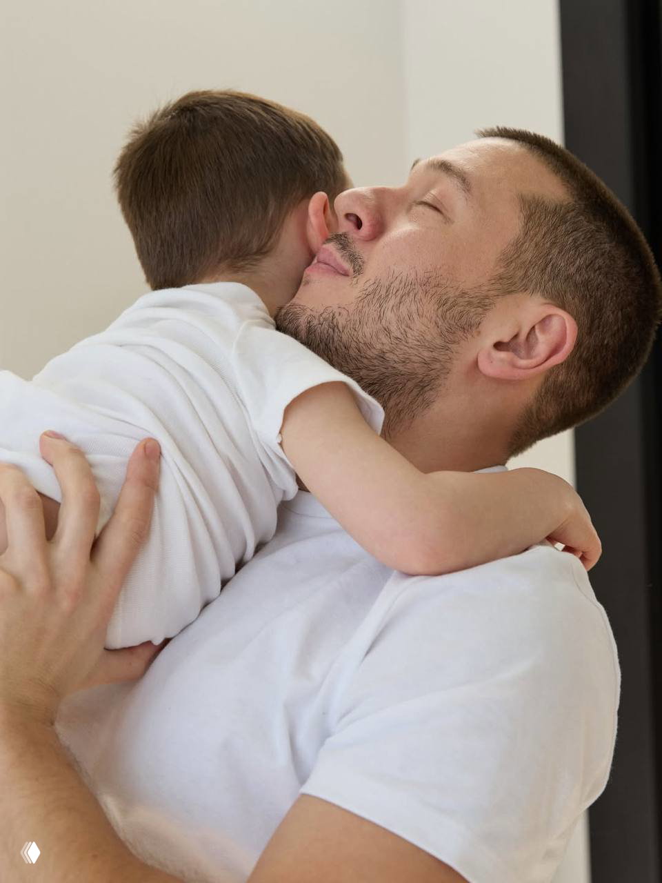 Крупный план: мужчина нежно обнимает ребёнка, прижимая к себе; кадр подчёркивает отцовскую ласку и уютную семейную атмосферу.