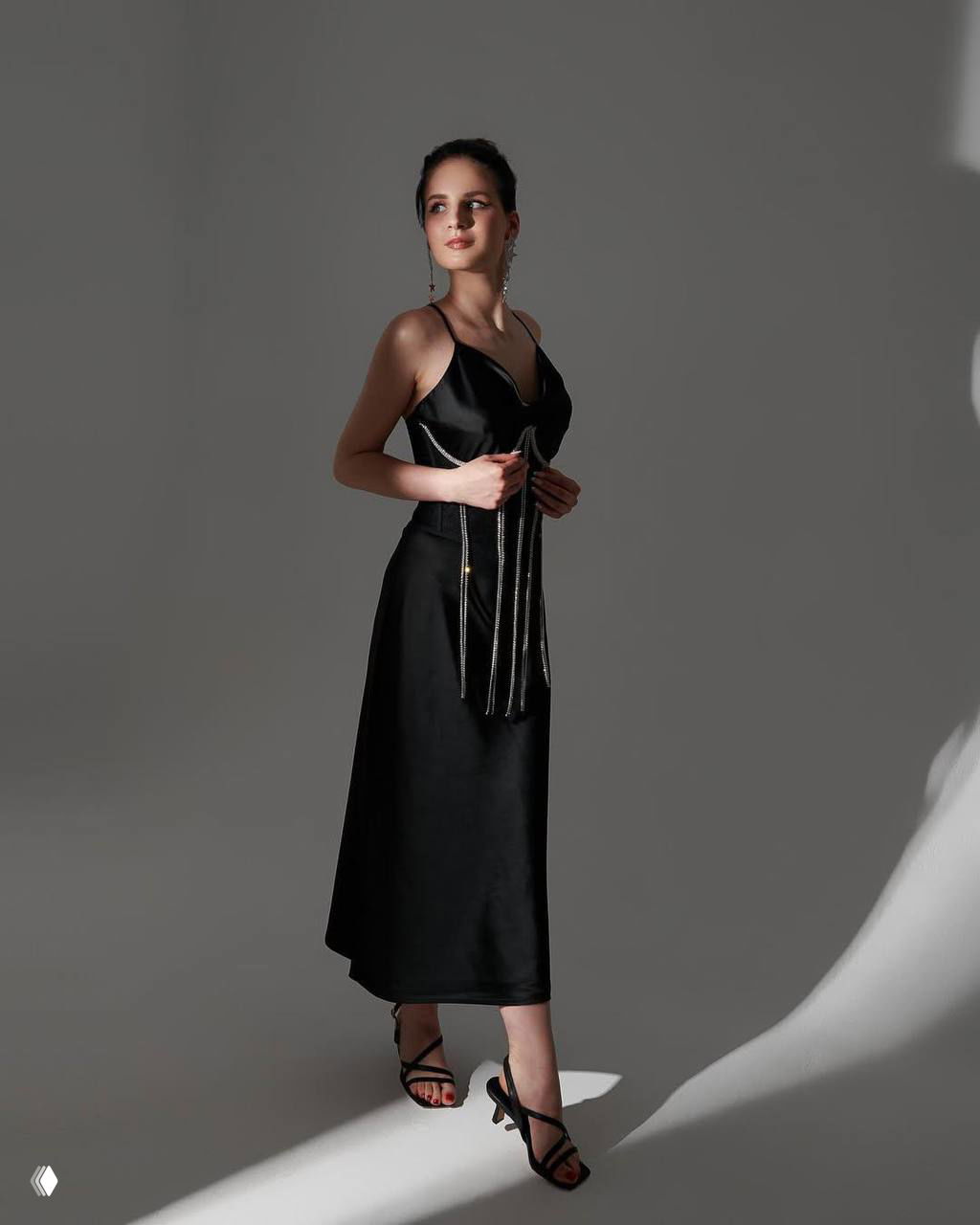 Девушка в чёрном вечернем платье позирует в студии на нейтральном фоне; элегантный портрет с художественным светом и длинной юбкой.