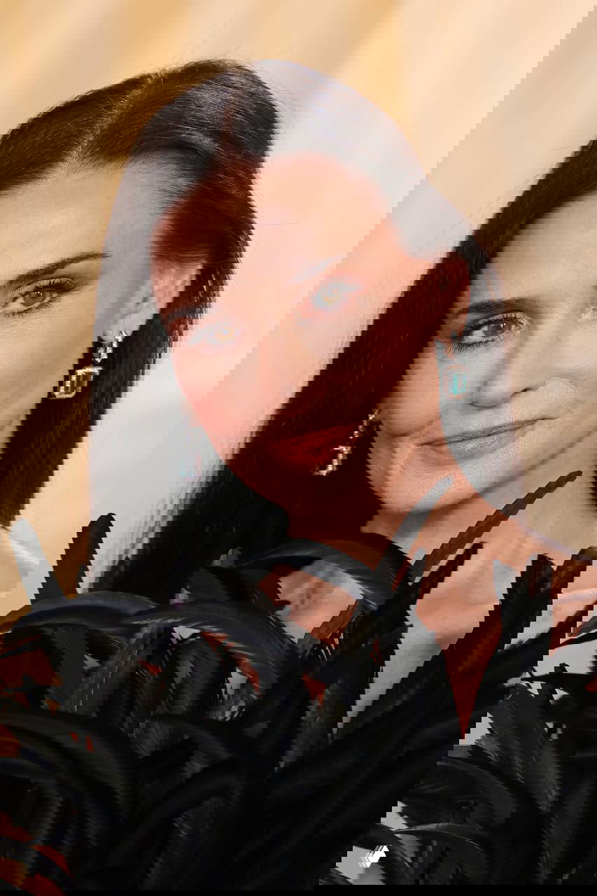 Крупный план лица актрисы и верхней части платья с перьями; видны серьги, макияж и текстура декоративной отделки наряда.