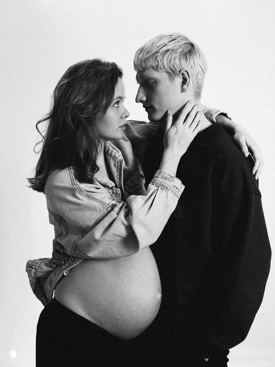 Студийное чёрно‑белое фото: беременная Мила Ершова со свободной рубашкой и оголённым животом в объятиях Святослава Рогожана, семейный снимок беременности.