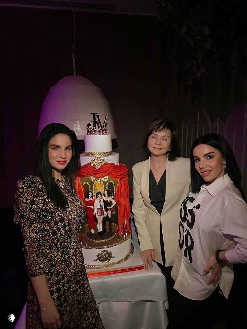 Три женщины рядом с большим праздничным тортом на вечернем приёме; кадр показывает атмосферу торжества и праздничный декор без указания имён.