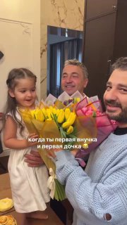 Маленькая девочка держит букет ярко‑жёлтых тюльпанов рядом со взрослыми — кадр семейного праздника и подарков в домашней обстановке