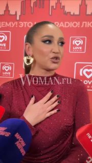 Ольга Бузова во время интервью на красной сцене; полубочный портрет с рукой на груди, в кадре микрофоны и фирменный фон мероприятия.
