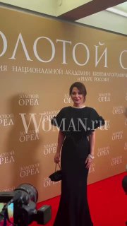 Екатерина Климова в длинном элегантном чёрном платье позирует на красной дорожке премии «Золотой орёл» со клатчем и жемчужным ожерельем.