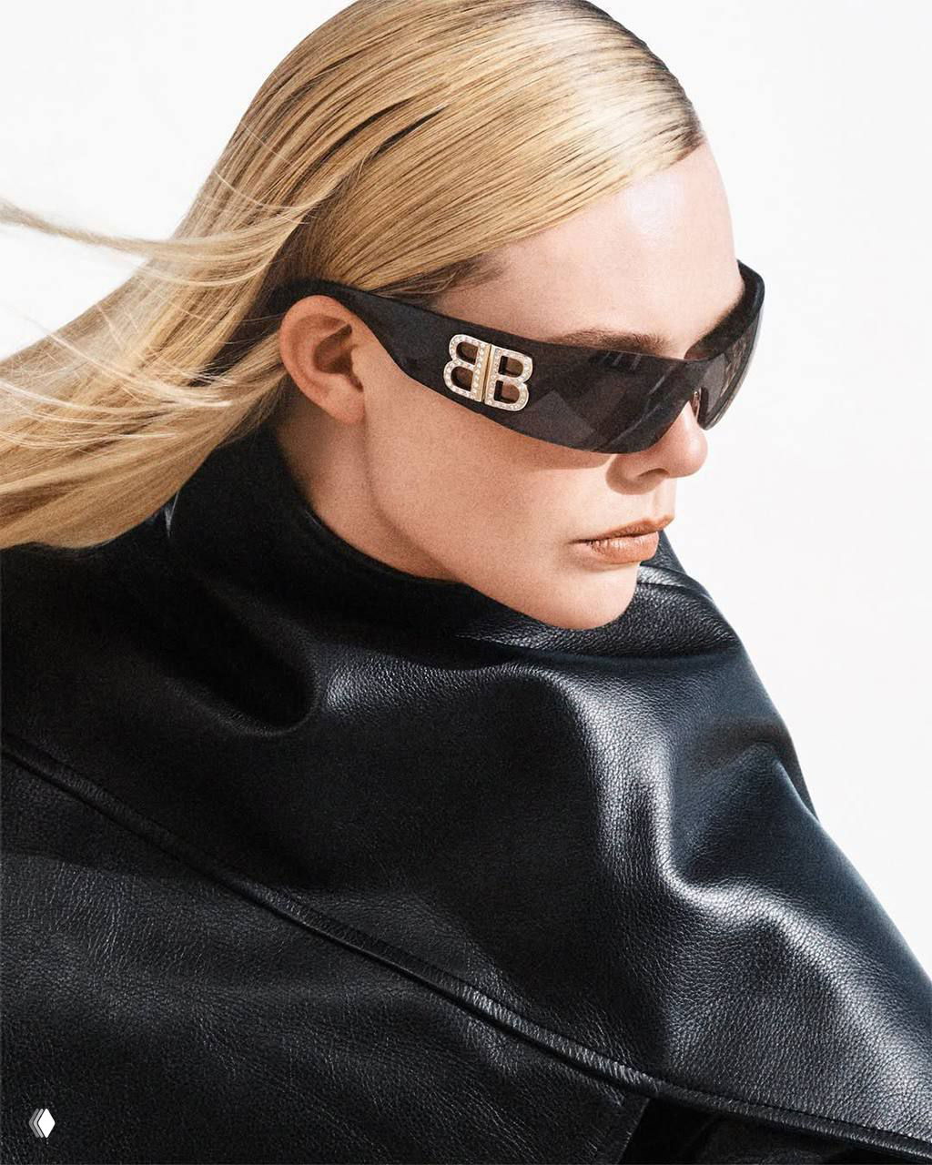 Крупный план женщины-модели в темных солнцезащитных очках с логотипом на дужке, строгая кожаная накидка и холодный свет — модная деталь съемки.